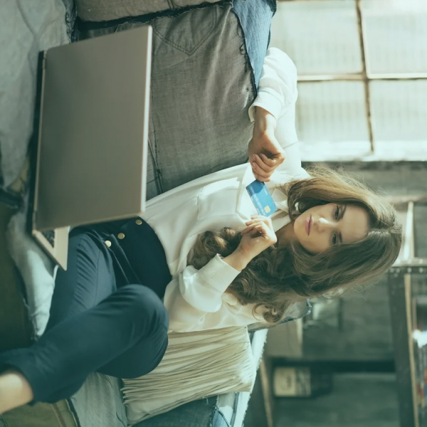 Девушка смотрит в ноутбук держа банковскую карточку